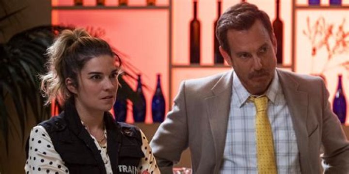 Annie Murphy and Will Arnett in a still from Murderville; the former undercover dressed like a man holding a box